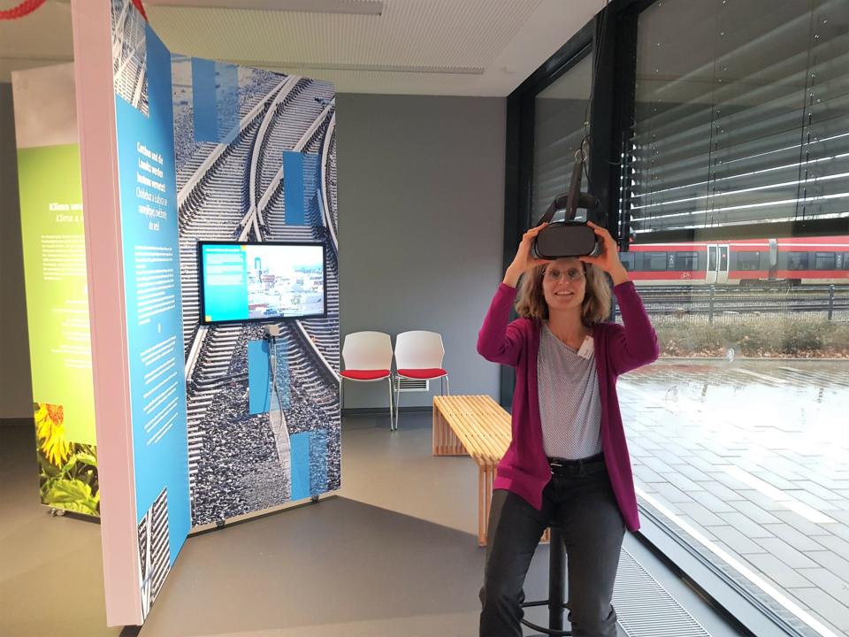 Fotografie (JB): Frau Breuß führt durch das Informationszentrum. Hier kann man per VR-Brille die ganze Stadt erkunden und dabei viel Wissenswertes zu den Strukturprojekten erfahren.